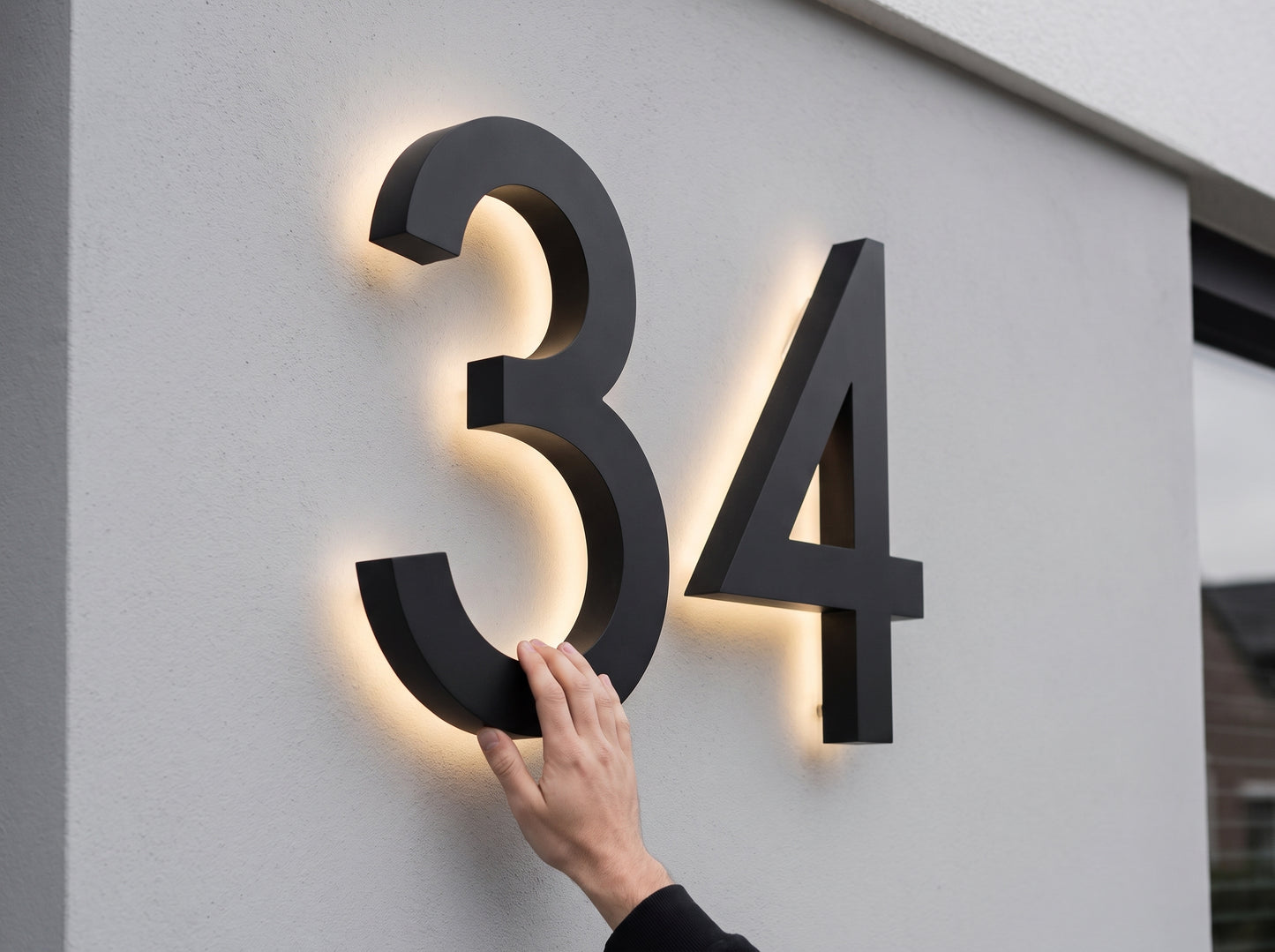 Dwie cyfry LED XL tworzące numer domu 34 na elewacji, dłoń pokazuje skalę
