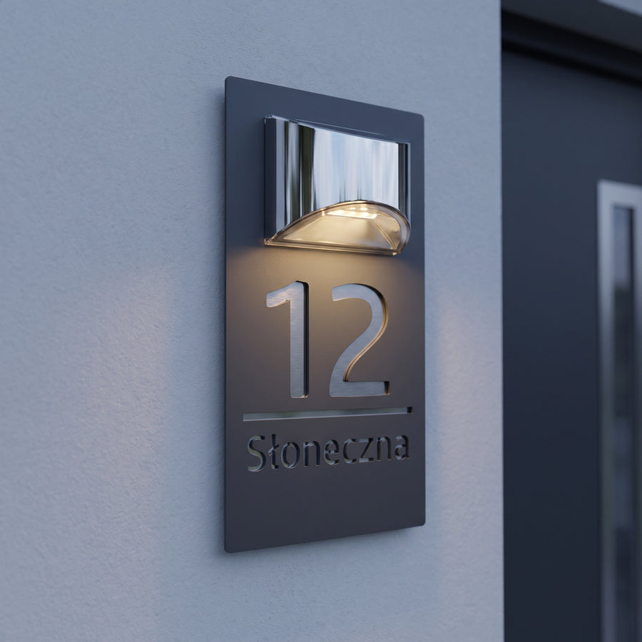 Solarna tabliczka adresowa 12 Słoneczna z chromowaną lampą solarną na jasnoszarej elewacji o zmierzchu
